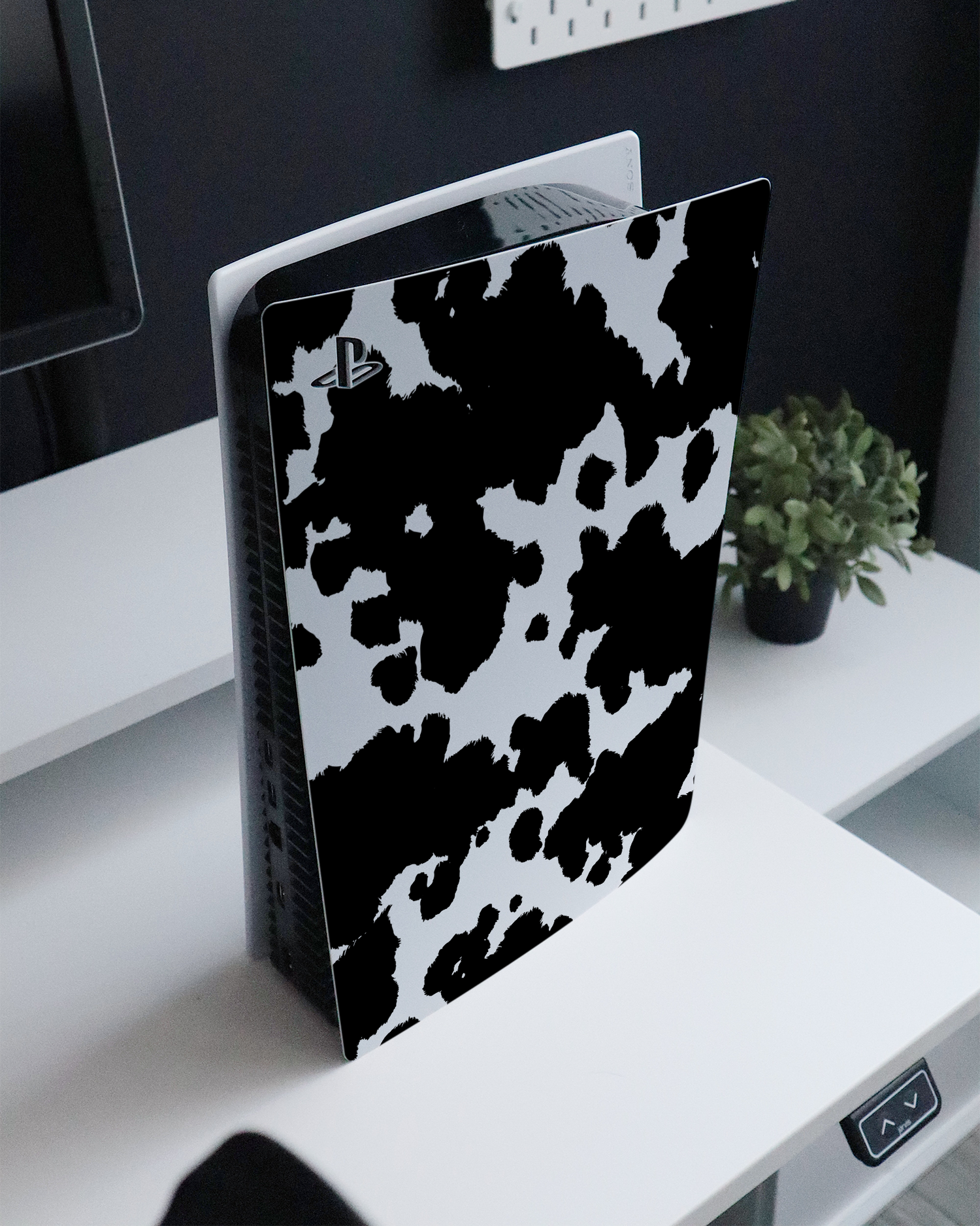 Cow Print Console Skin for Sony PlayStation 5 standing on a sideboard 